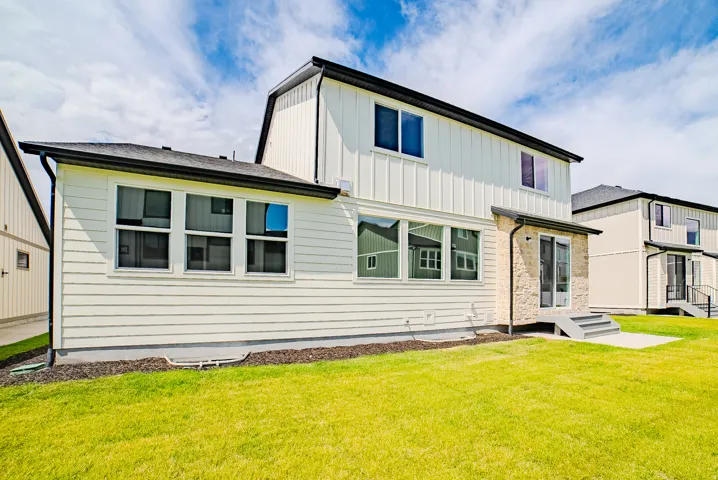 Exterior featuring white siding, black-framed windows, a stone accent wall, and a concrete patio
