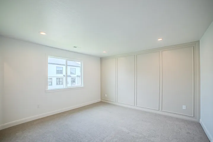 Recessed ceiling lighting, white walls, gray carpet, single window with white trim, and decorative wall paneling