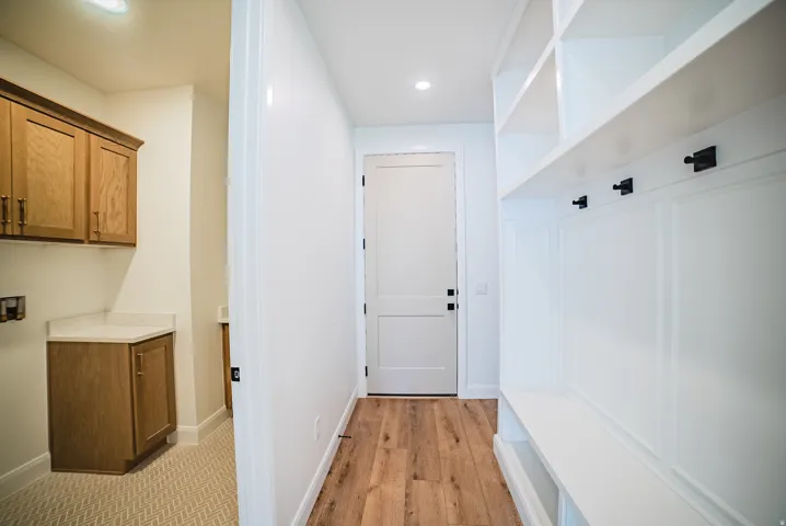 Built-in mudroom bench with storage and hooks, white two-panel interior doors, wood-finish flooring, recessed lighting, and laundry area with wood cabinetry and light-toned countertop