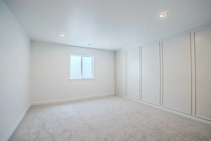 Recessed lighting, textured carpet flooring, window with white trim, and a decorative paneled accent wall