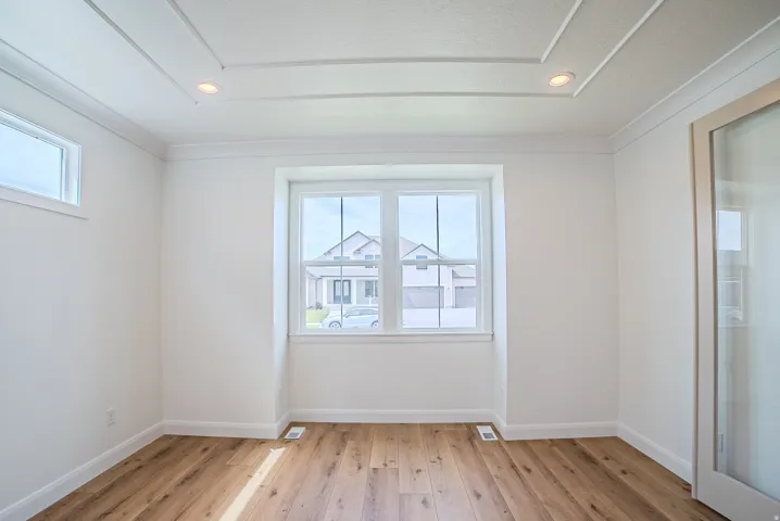 Wood-finish flooring with white baseboards, a large central window, and an upper transom window