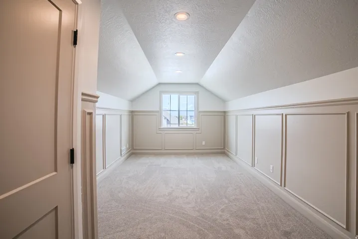 Vaulted ceiling, recessed lighting, window with trim, decorative wainscoting, and carpeted flooring