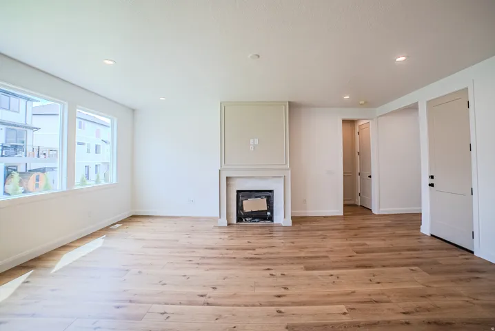 Spacious room featuring wood-finish flooring, recessed lighting, multiple windows, a decorative fireplace with mantel, and contemporary two-panel doors