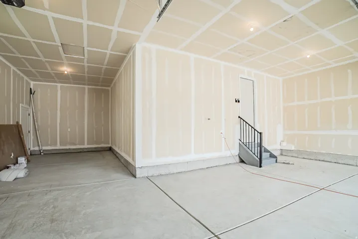 Unfinished garage space featuring exposed drywall, a concrete floor, and integrated ceiling lighting