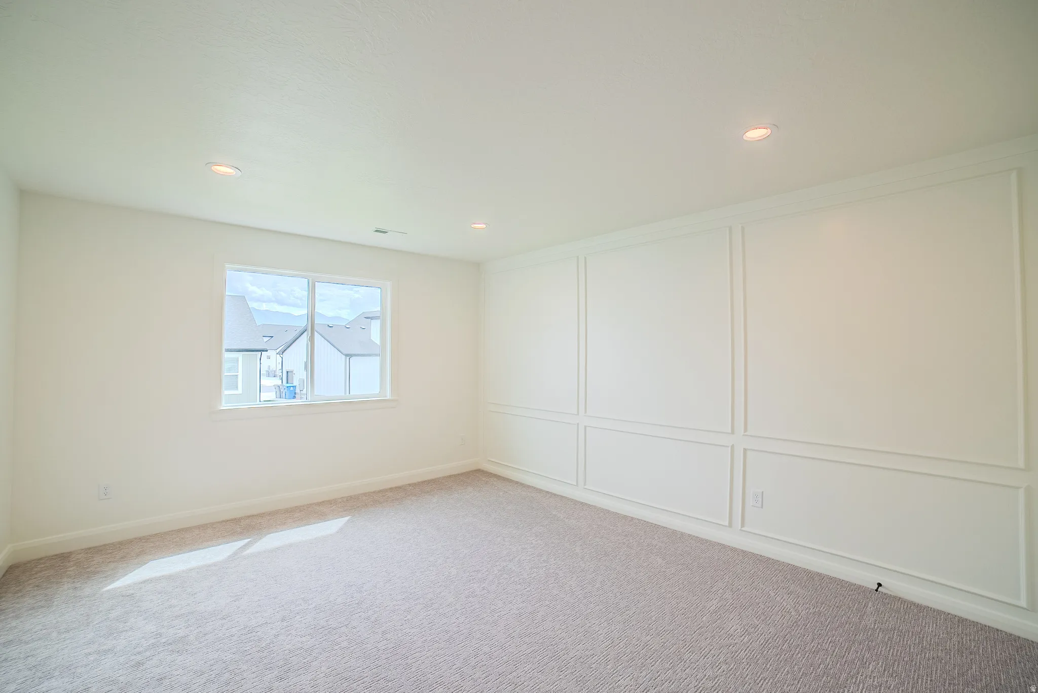 Recessed lighting, large window, paneled accent wall, and neutral-toned carpeting