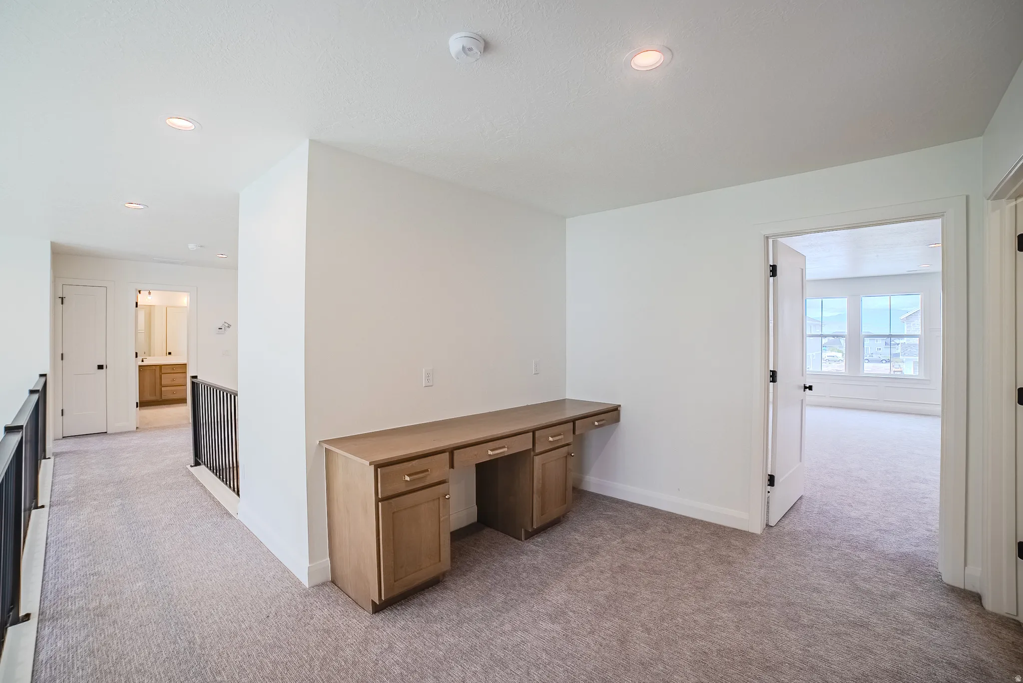 Integrated built-in desk with wood-finish cabinetry, neutral carpeting, recessed ceiling lighting, and crisp white walls