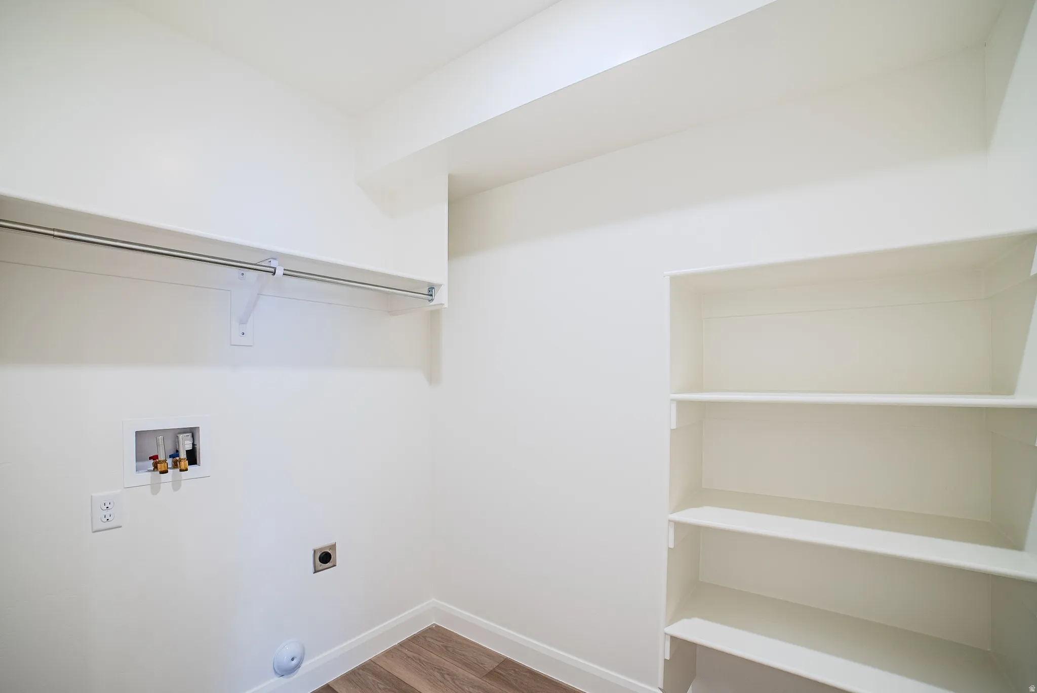Dedicated laundry space featuring a built-in hanging rod, integrated shelving, wood-finish flooring, and bright white walls