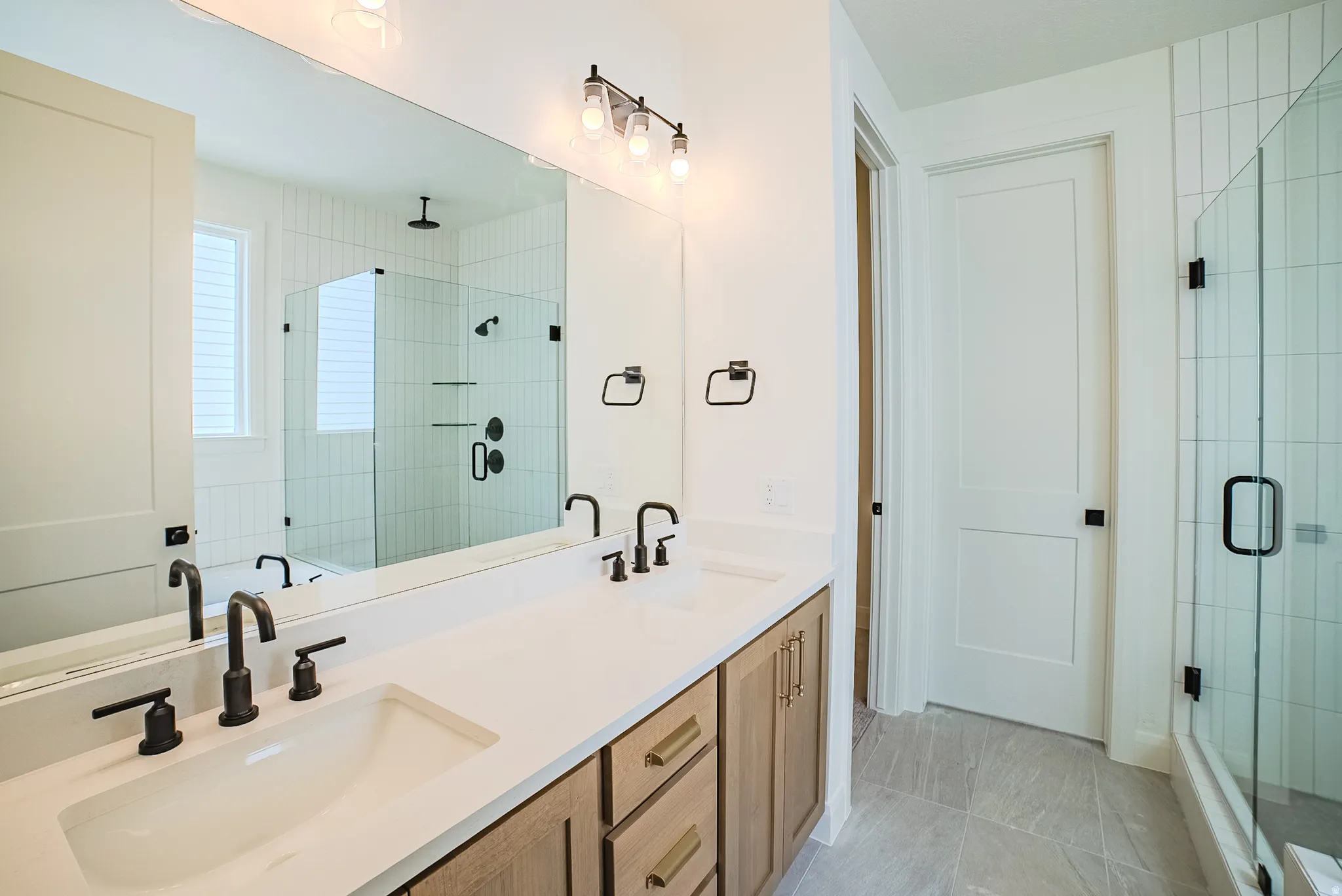 Double vanity with integrated sinks, matte black fixtures, and light wood-finish cabinetry