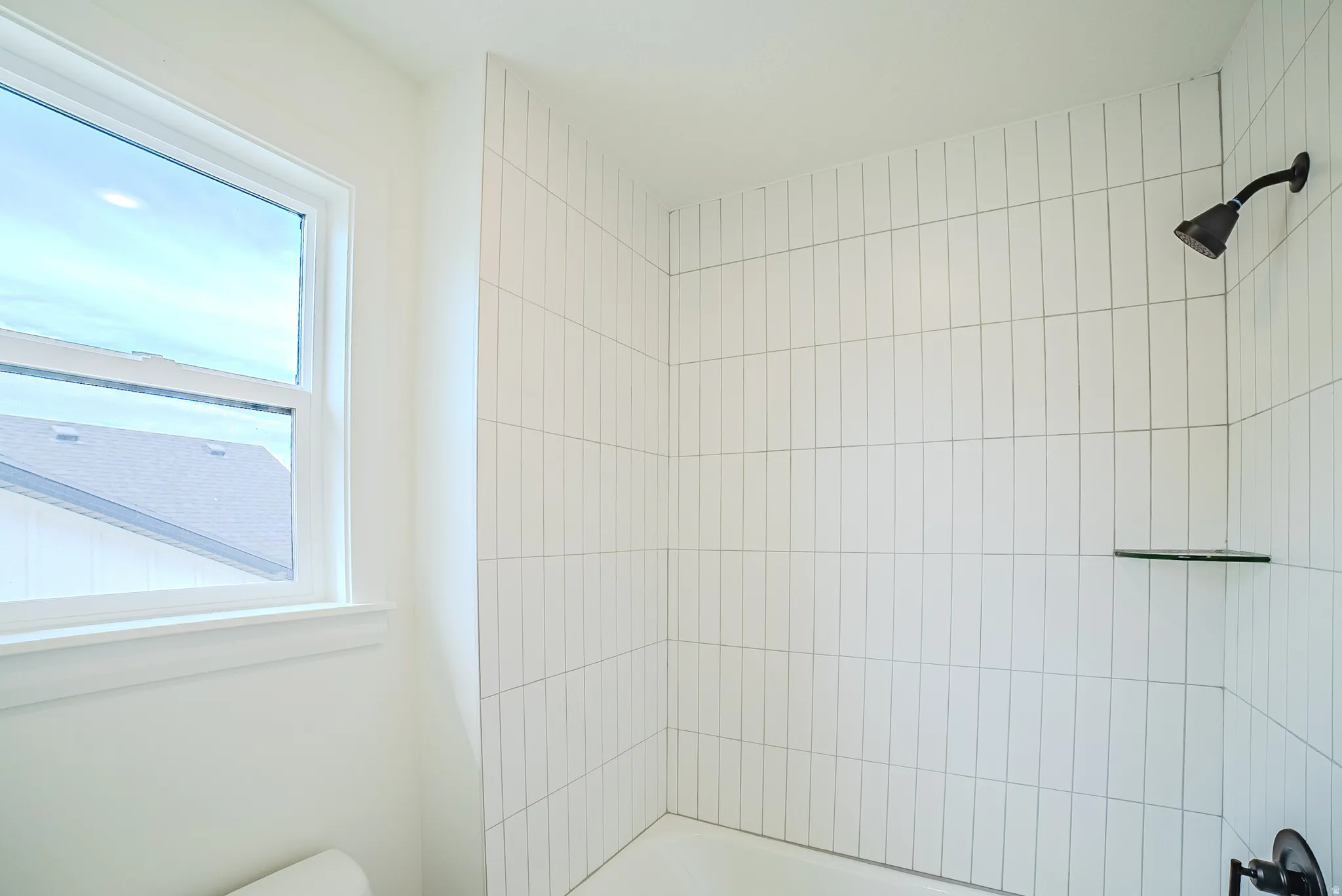 White vertical tile shower surround with a matte black shower head and a built-in glass shelf