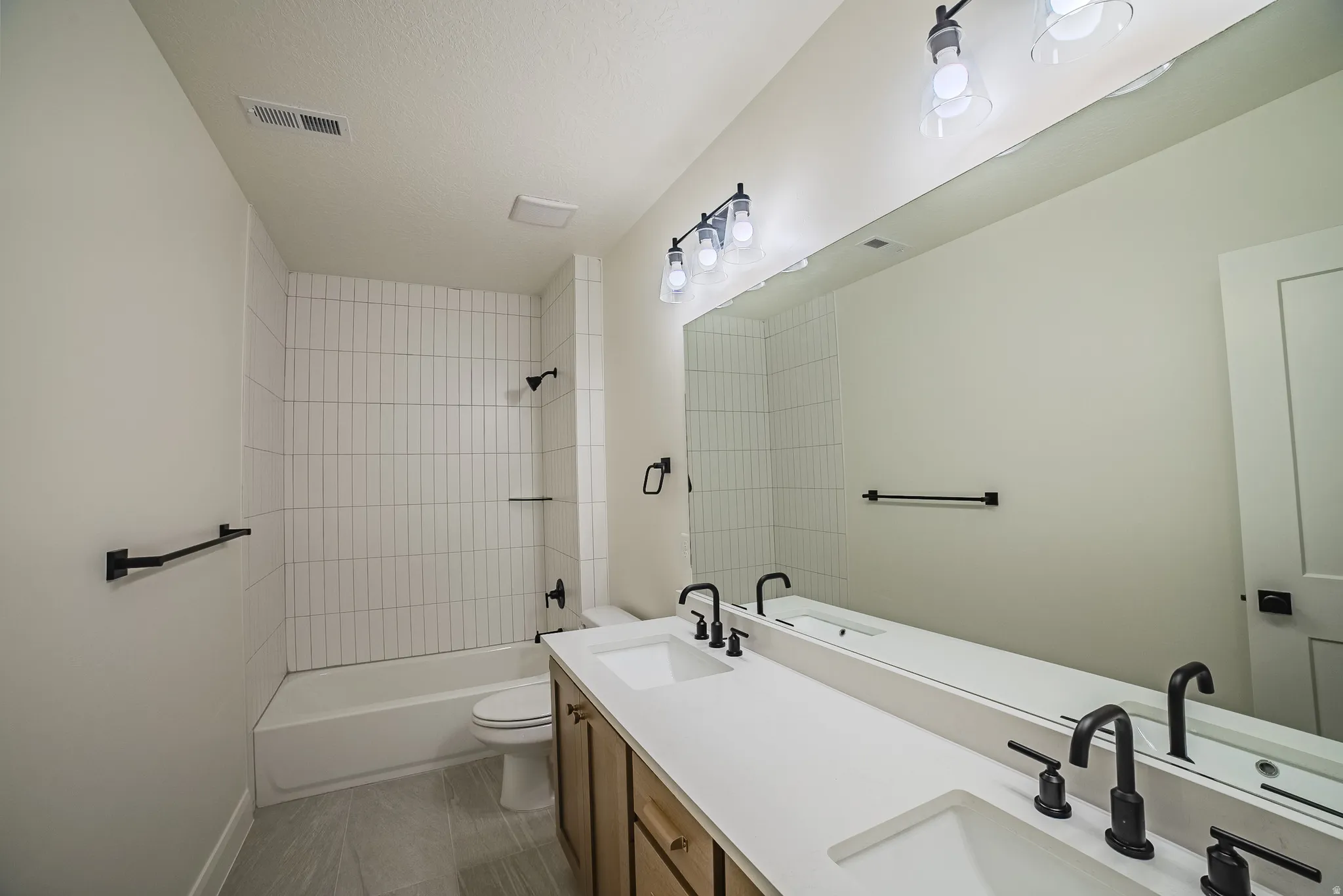 Dual vanity with integrated sinks, matte black fixtures, full-width mirror, and a tub/shower combination with vertical tile surround