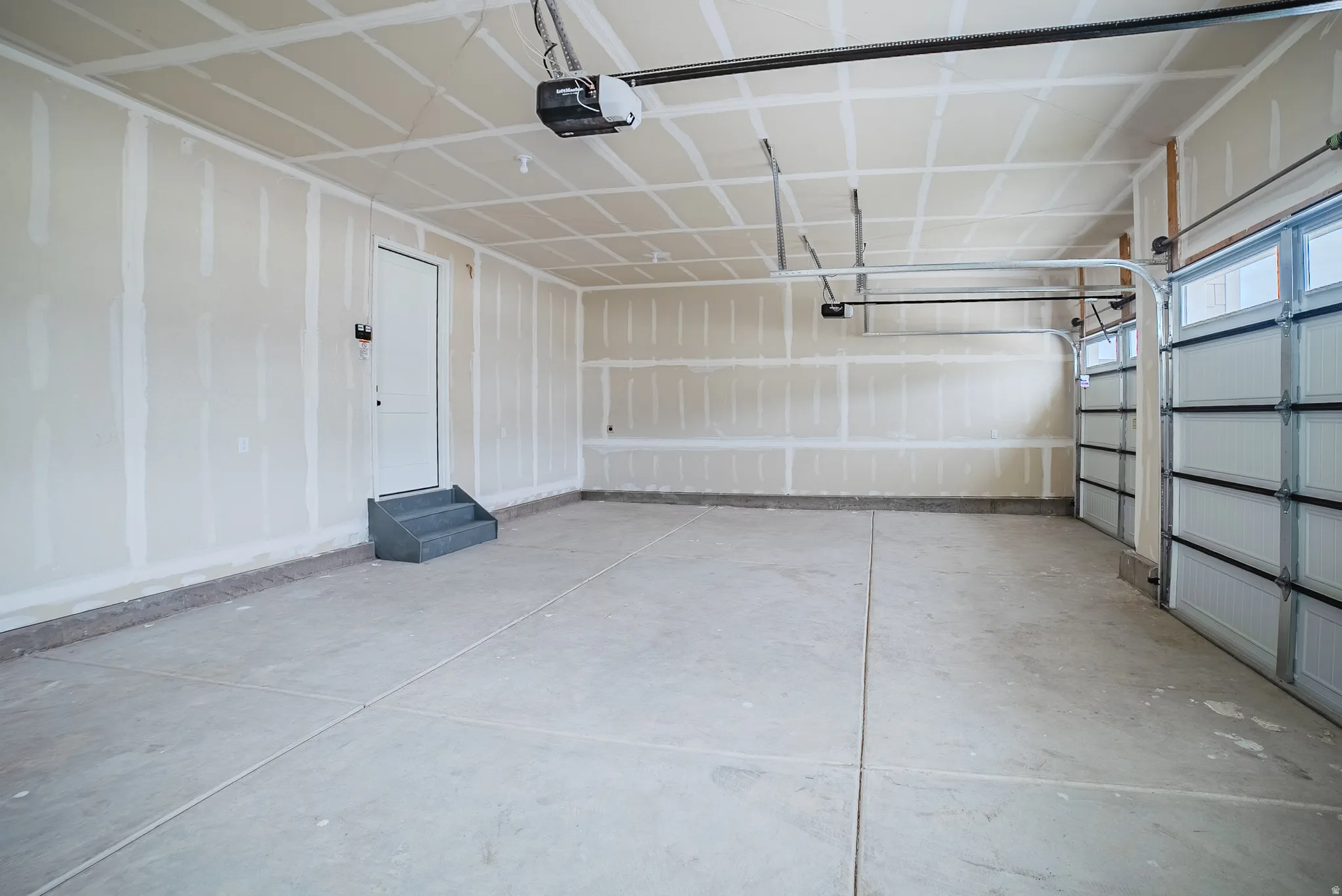 Spacious garage featuring a concrete floor, overhead door opener, and interior access door with steps