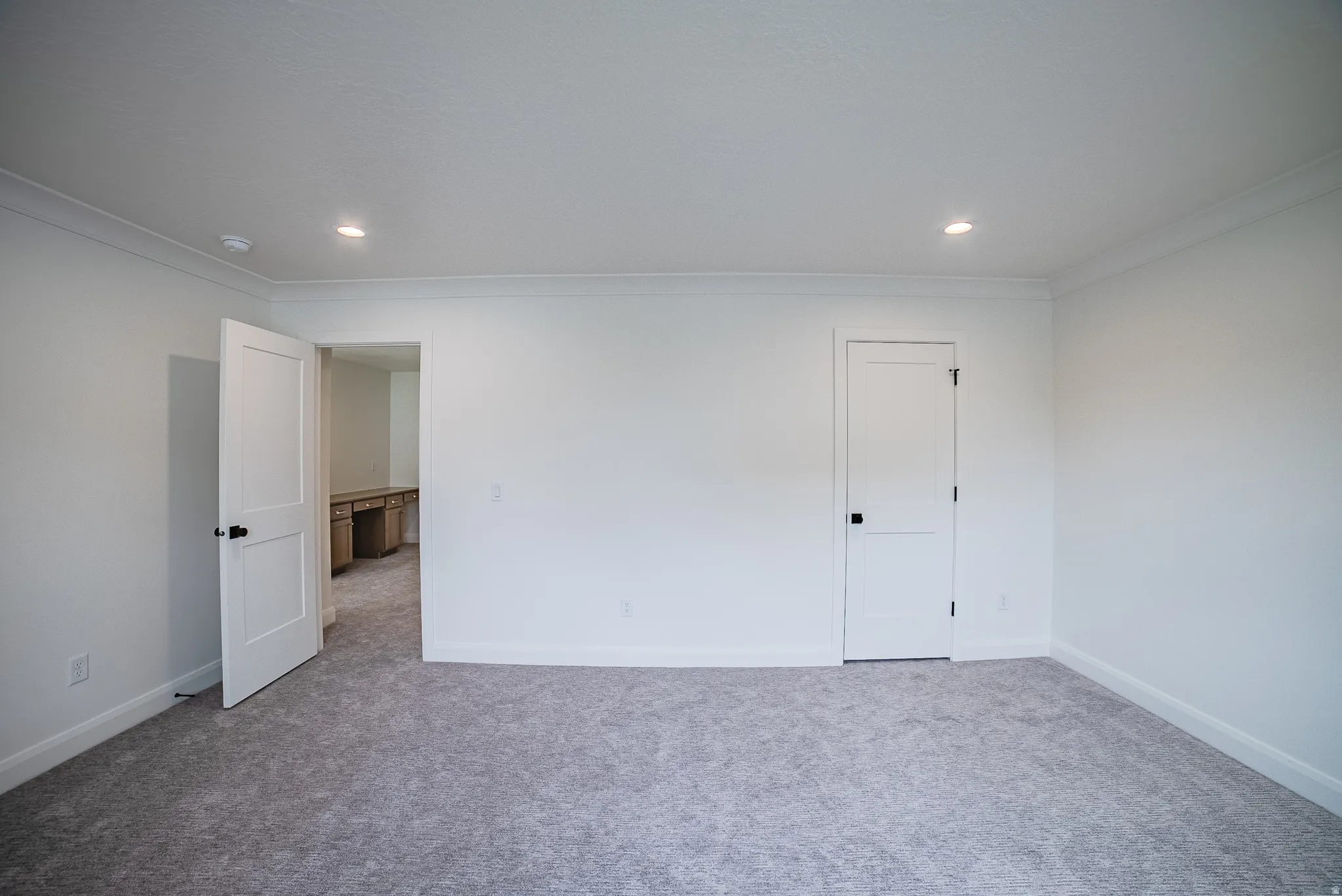 Neutral-toned carpet flooring, recessed ceiling lighting, crown molding, white paneled doors, and matte black hardware