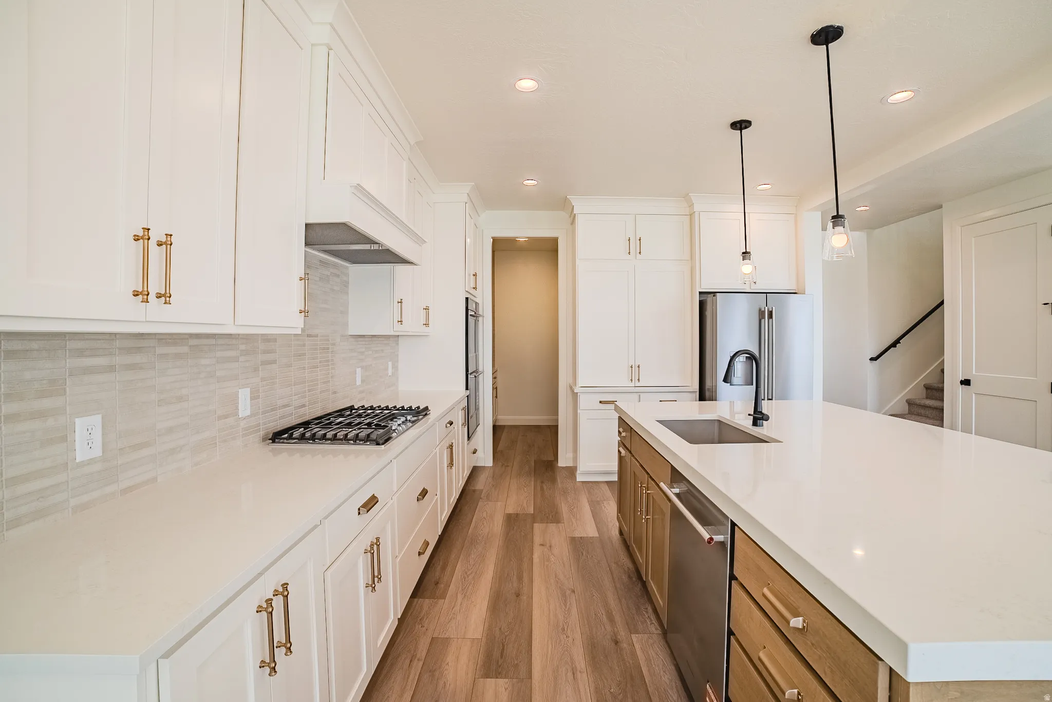 White shaker cabinetry with brass-finish hardware, stainless steel appliances, wood-finish flooring, and a central island with an undermount sink