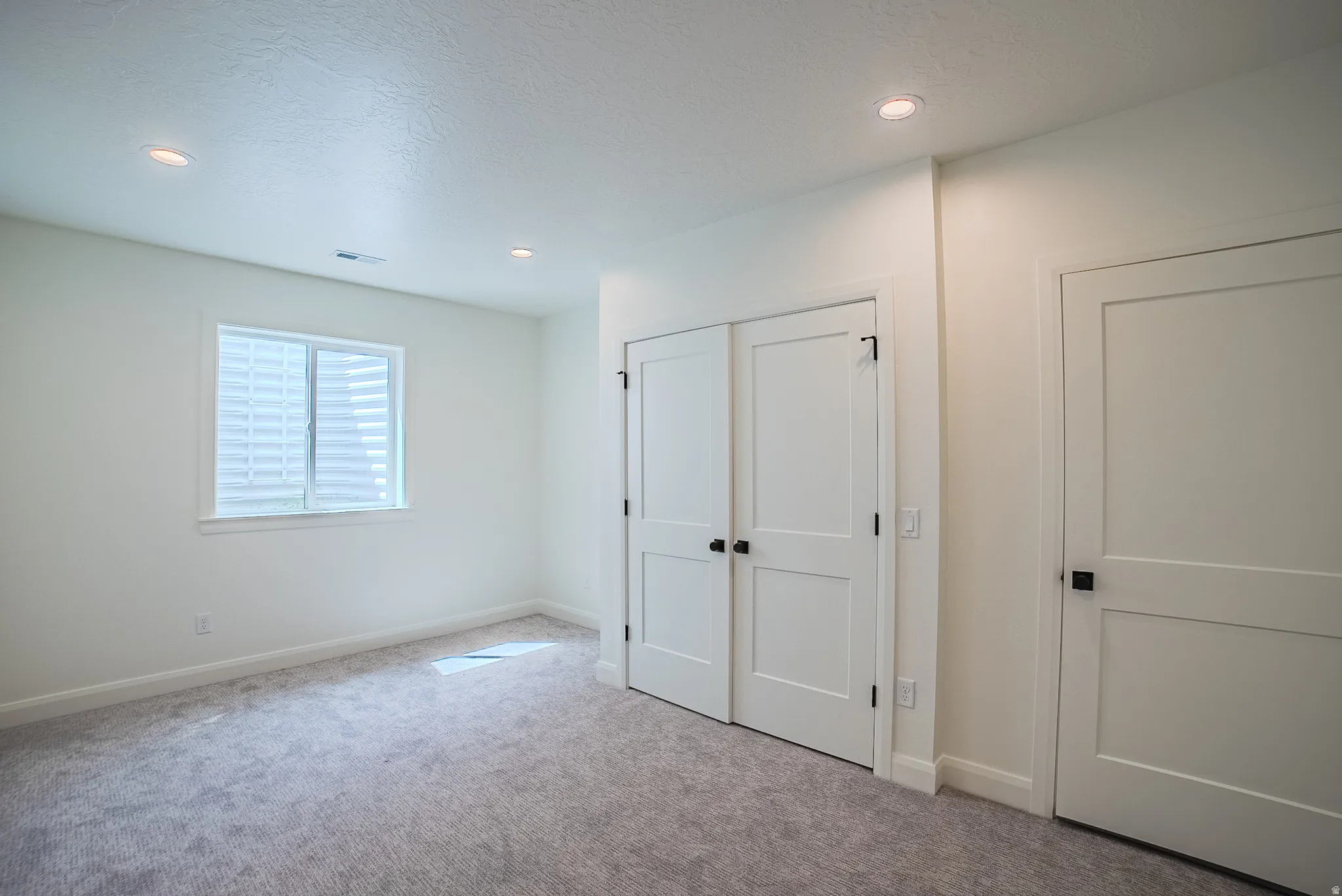 Recessed lighting illuminates the room with neutral carpeting