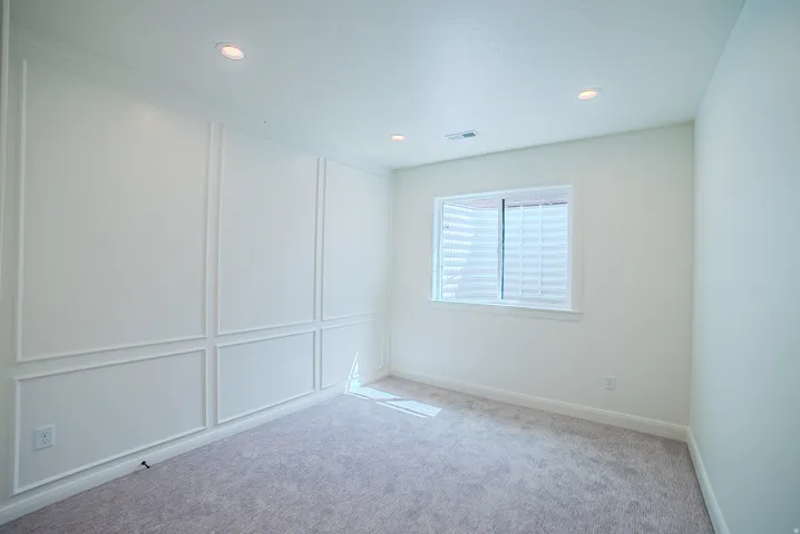 Recessed lighting, window with horizontal blinds, decorative wall paneling, light-toned carpet flooring, and white walls