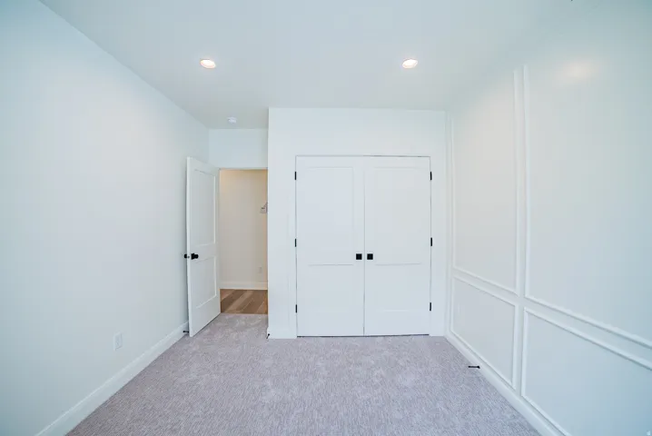 Recessed lighting, light gray carpet, white walls, white paneled double doors, decorative wall molding