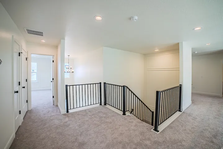 Carpeted hallway with black wrought iron railing, recessed lighting, and white paneled doors