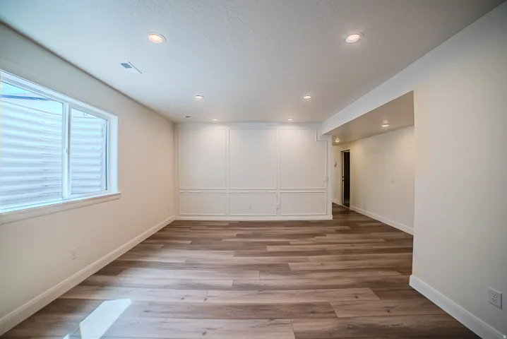 Recessed lighting illuminates the wood-finish flooring, complemented by a decorative wall panel accent and a large window