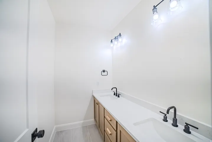 Double vanity with integrated sinks and white countertops, natural wood-finish cabinetry, and matte black fixtures