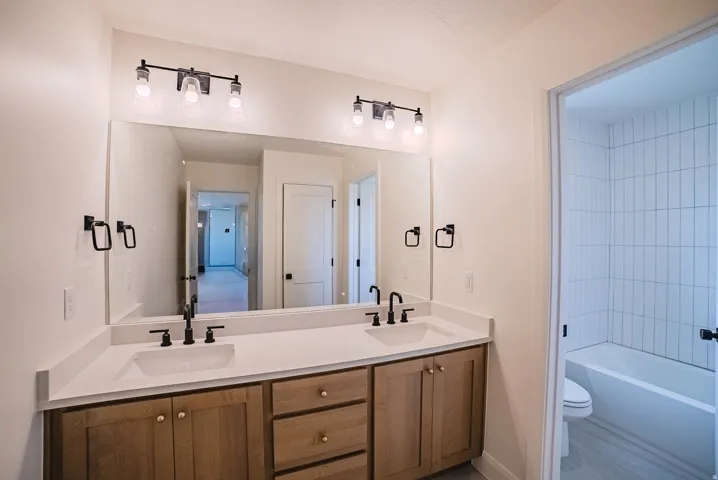 Dual vanity with stone countertops, wood-finish cabinetry, and matte black fixtures
