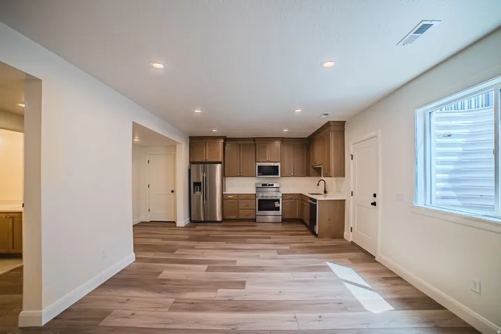 Open-concept living area with wood-finish flooring, recessed lighting, and a kitchen featuring stainless steel appliances, light wood cabinetry, and white countertops