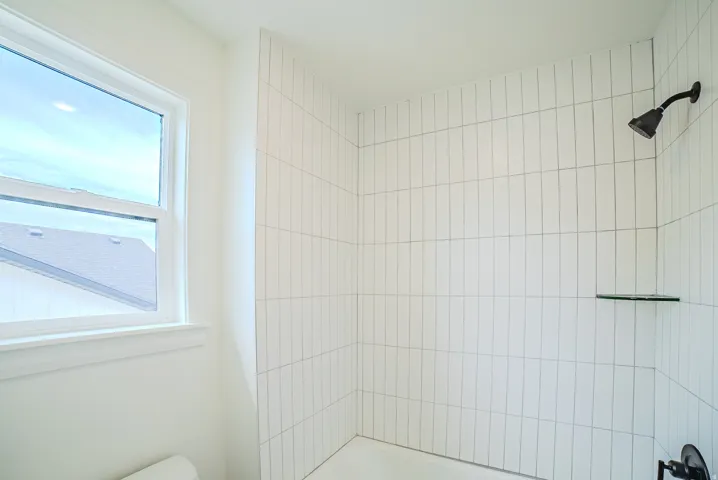 White vertical tile shower surround with a matte black shower head and a built-in glass shelf
