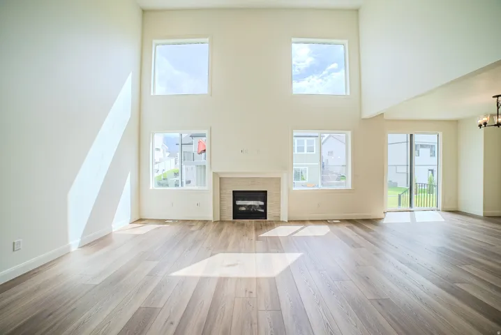 Soaring vaulted ceilings with multiple windows, wood-finish flooring, fireplace with a mantle, and sliding glass door