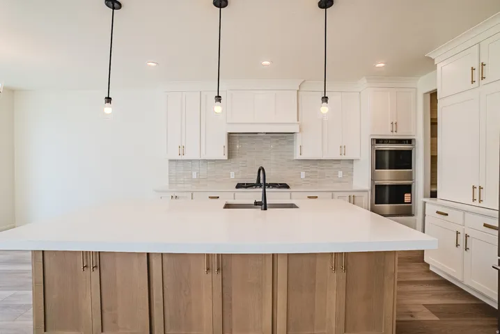 Kitchen featuring a large central island with light wood-finish cabinetry, white countertops, and a built-in stainless steel double oven