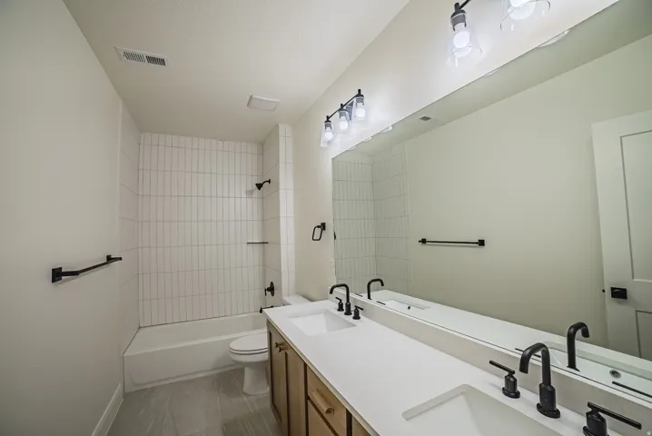 Dual vanity with integrated sinks, matte black fixtures, full-width mirror, and a tub/shower combination with vertical tile surround
