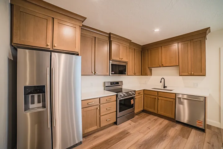 L-shaped kitchen featuring wood-finish cabinetry, stainless steel appliances, white countertops, a black gooseneck faucet, and wood-finish flooring