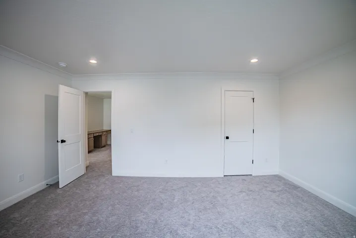 Neutral-toned carpet flooring, recessed ceiling lighting, crown molding, white paneled doors, and matte black hardware