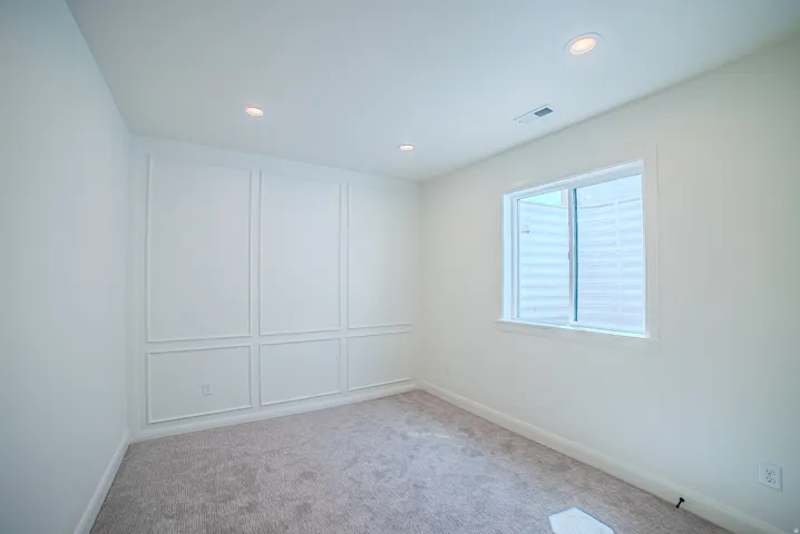 Recessed lighting, wall paneling, window, light gray carpeting, and white walls