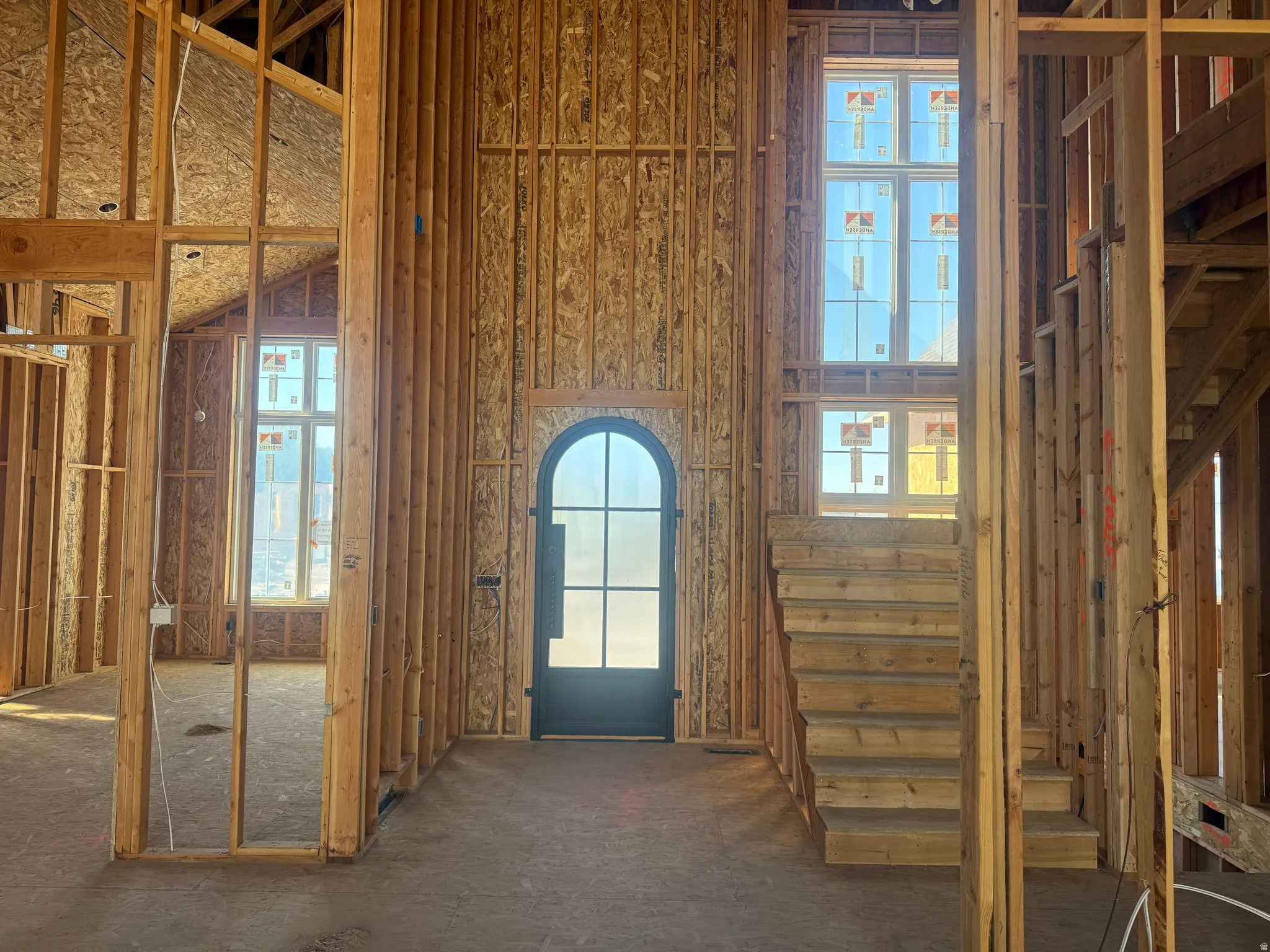 Double-height entryway with an arched glass-paneled door, tall windows, and a prominent staircase