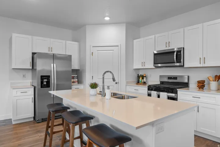 Kitchen featuring white cabinetry, stainless steel appliances, a center island with sink, light-toned countertops, and wood-finish flooring