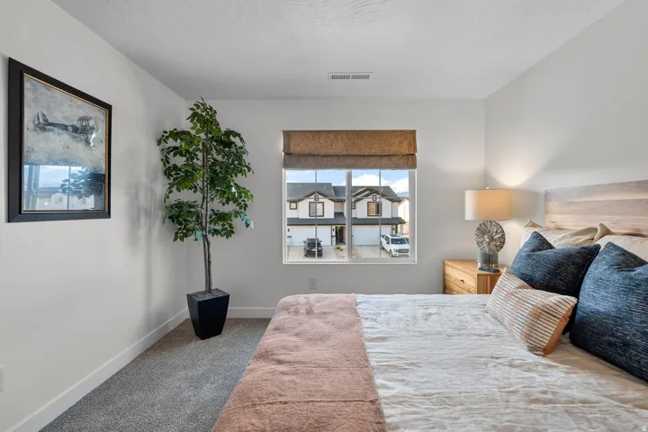 Textured carpet flooring, window with a privacy shade, natural wood headboard, and a wood-finish nightstand