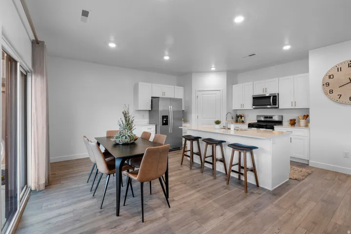 White cabinetry, stainless steel appliances, wood-finish flooring, recessed lighting, and a kitchen island with seating
