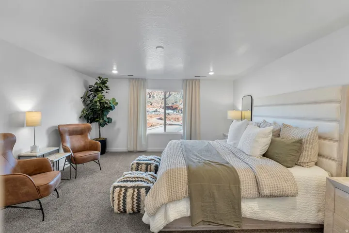 Recessed ceiling lighting, large window with outdoor scenery, light-colored walls, carpeted flooring, and a contemporary padded headboard