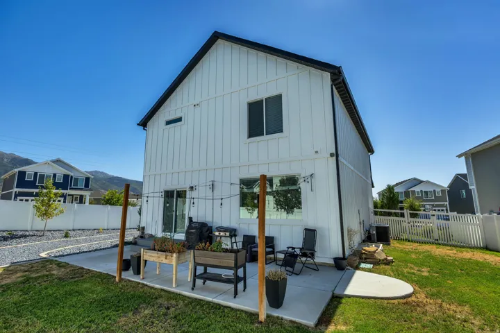 Board and batten siding, black trim accents, concrete patio, sliding glass door, and a white picket fence
