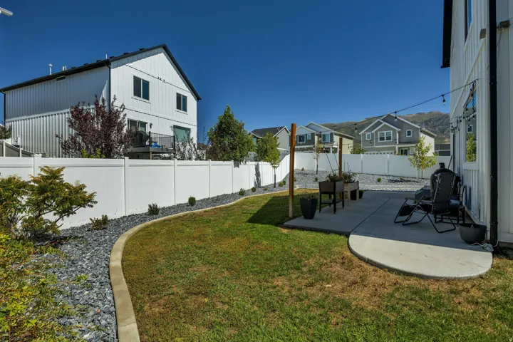 Expansive grass yard with a curved concrete patio, surrounded by a white privacy fence, and featuring decorative stone landscaping