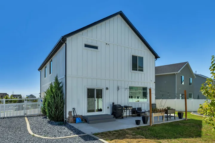 White board and batten exterior with black trim, concrete patio, gravel border, and a white picket fence