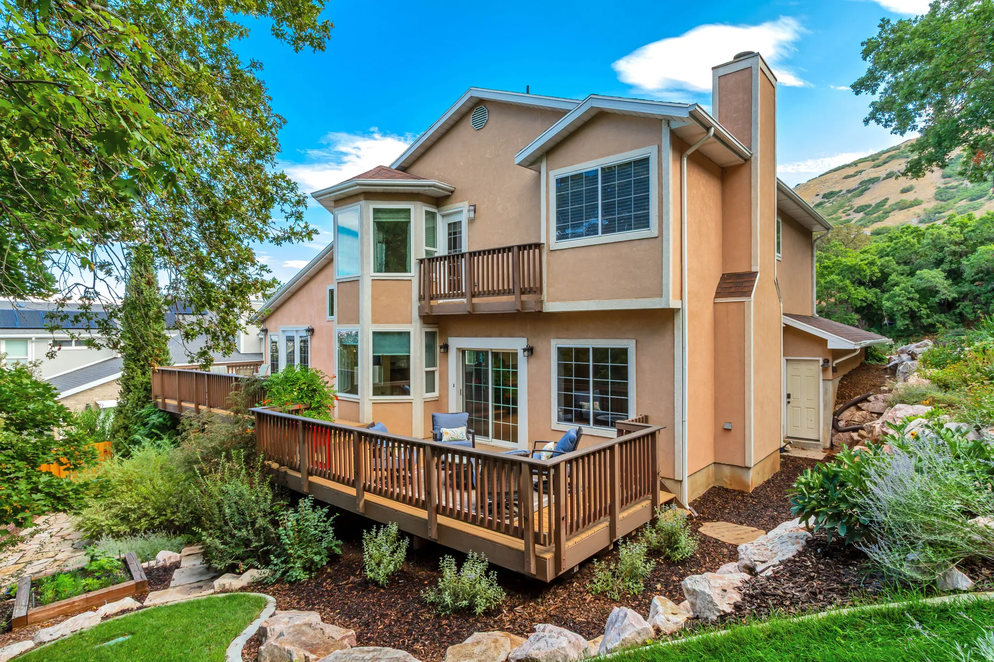 Multi-level wooden decks with baluster railings, stucco exterior, multiple large windows, and a prominent chimney feature
