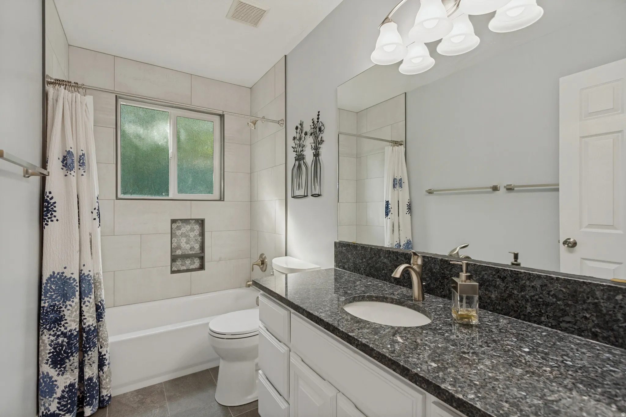 Bathroom featuring a dark speckled countertop, white cabinetry, undermount sink, and a framed mirror