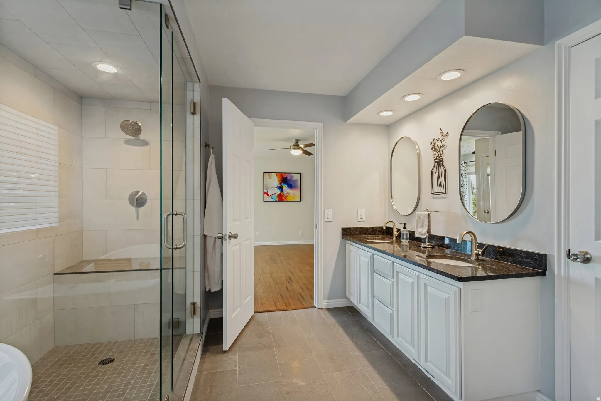 Dual vanity with individual oval mirrors, recessed lighting, white cabinetry, and a dark countertop