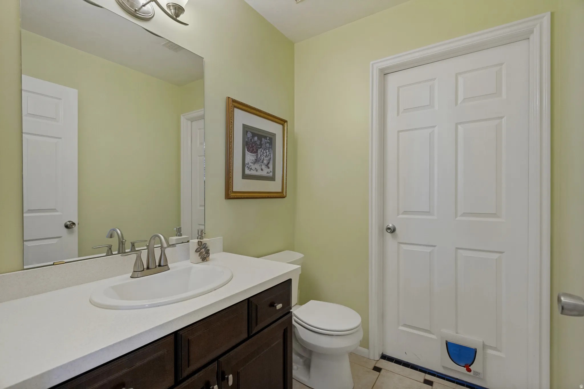 Vanity with a white countertop and dark wood-finish cabinetry, an undermount sink with a brushed nickel faucet, and a wall-mounted mirror