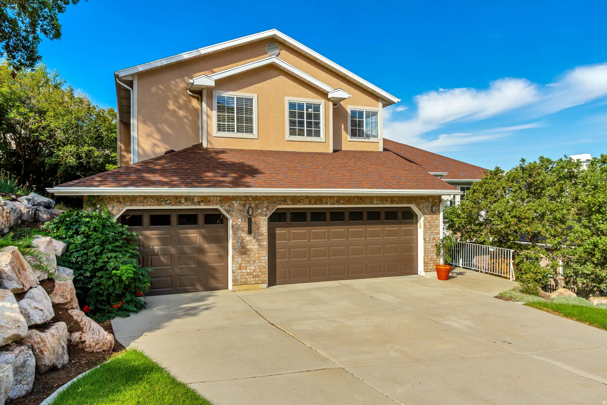 Two-story stucco and brick exterior with a multi-car garage, concrete driveway, and mature landscaping
