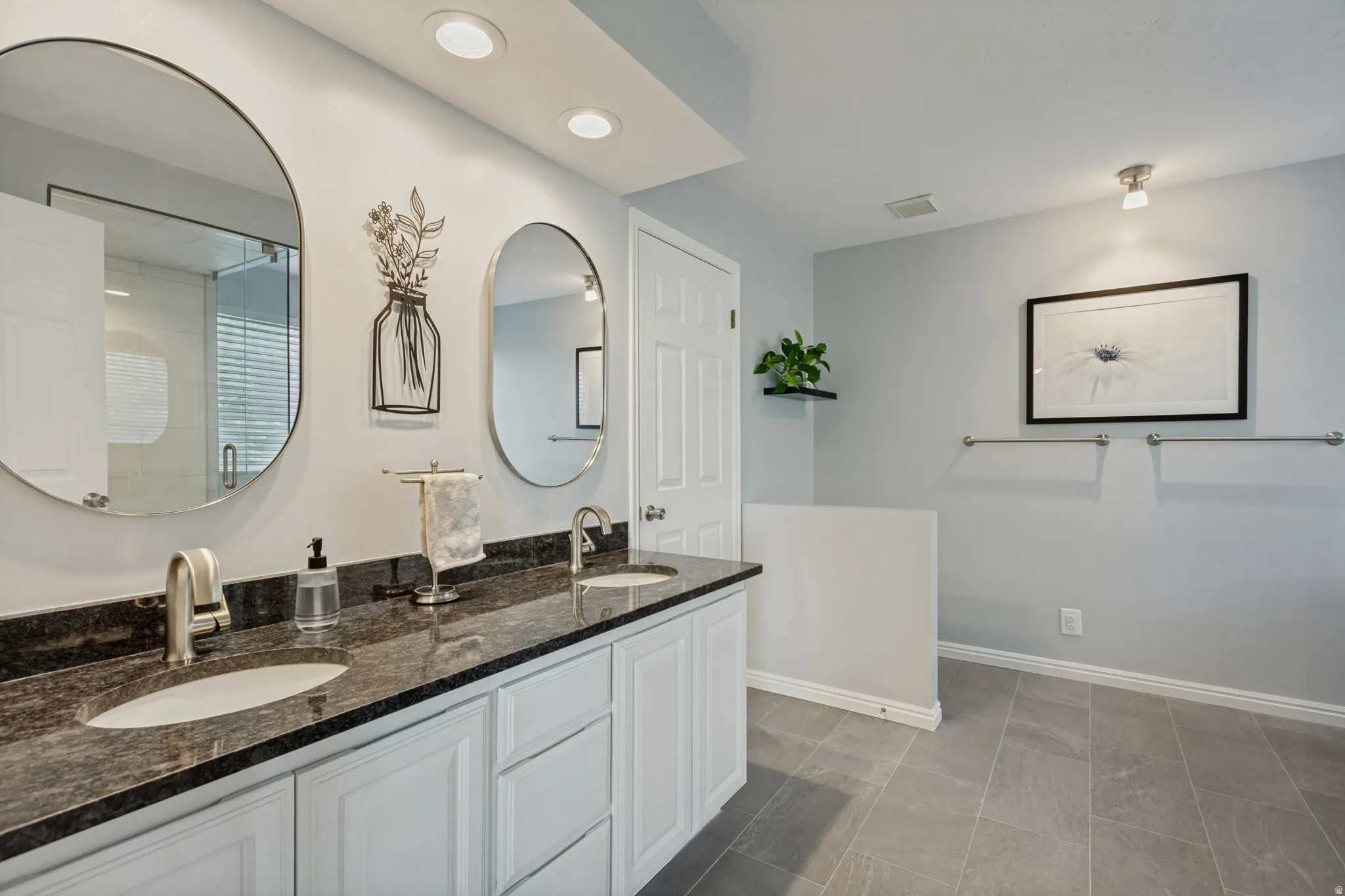 Dual vanity with dark stone countertop, undermount sinks, and white cabinetry