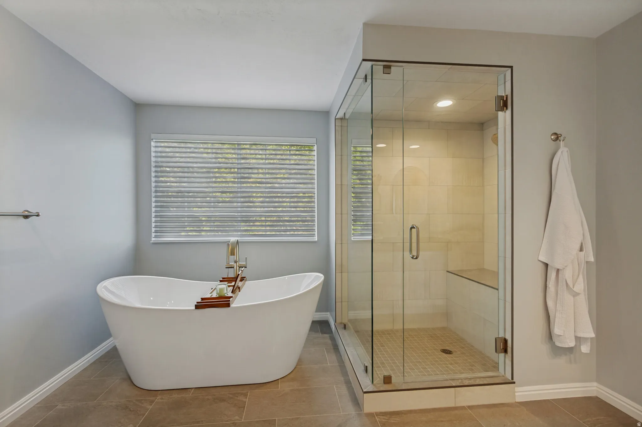 Freestanding soaking tub, glass-enclosed shower with a built-in bench, and large format tile flooring