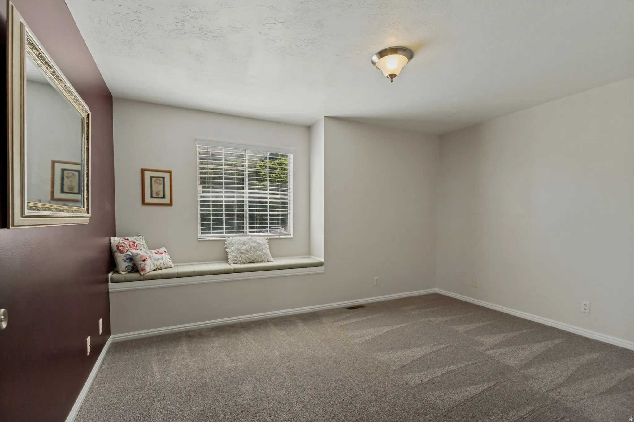 Recessed window seat with cushion, window with horizontal blinds, overhead ceiling light fixture, and neutral carpet