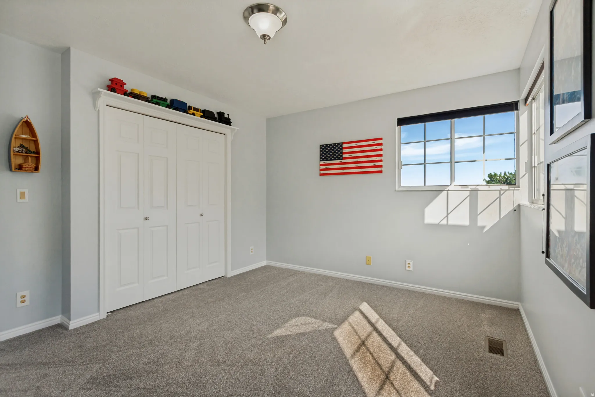 Window with horizontal blinds, neutral carpet flooring, and white bi-fold closet doors with detailed trim