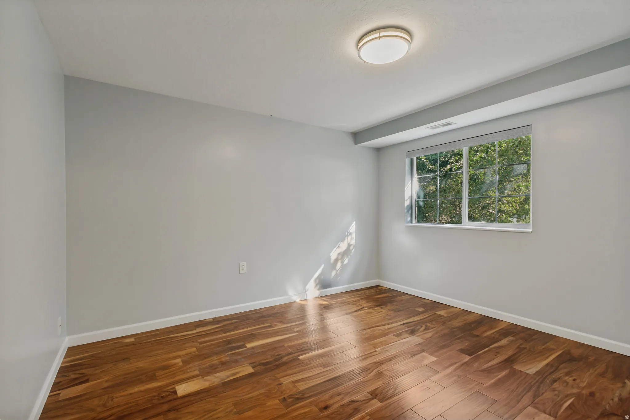 Wood-finish flooring, white trim, recessed window, and flush-mount ceiling light fixture